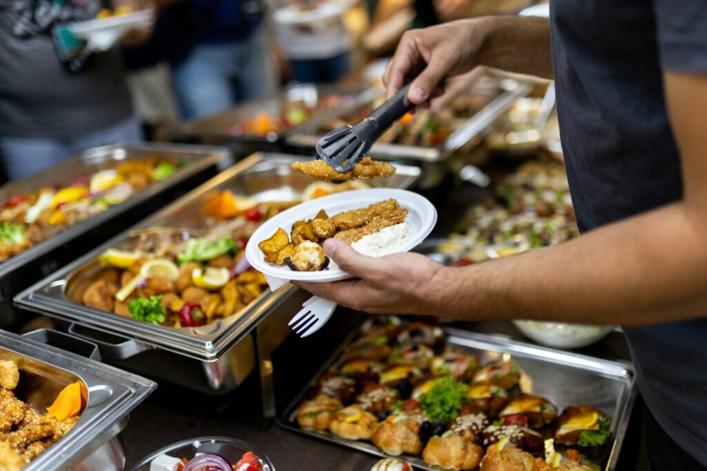 Person serving food from a buffet line using black tongs.